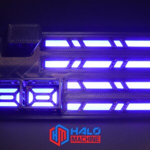 May include: A black rectangular device with blue neon lights. The device has multiple illuminated sections and the text "HALO MACHINE" in red and white. The device has a futuristic design.