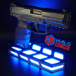 May include: A black handgun is displayed on a platform with bright blue lights. The platform has a geometric design. The words "HALO MACHINE" are in red and blue. The background is dark.