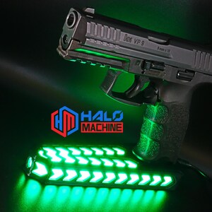 May include: A black handgun with the text "VP 9" and "9 mm x 19" is illuminated with green lights. Below the gun is a green LED light bar with arrow designs. The logo "HALO MACHINE" is visible in red and blue.