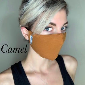 May include: A woman wearing a camel-colored face mask with the word "COMFY" printed on the side. The mask is made of a soft, breathable fabric.