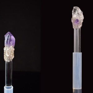 Puede incluir: Dos varitas de cristal con varillas transparentes y adornos de metal plateado. Una varita presenta un cristal de amatista p&uacute;rpura, la otra un cristal de cuarzo transparente. Ambas sobre fondo negro.