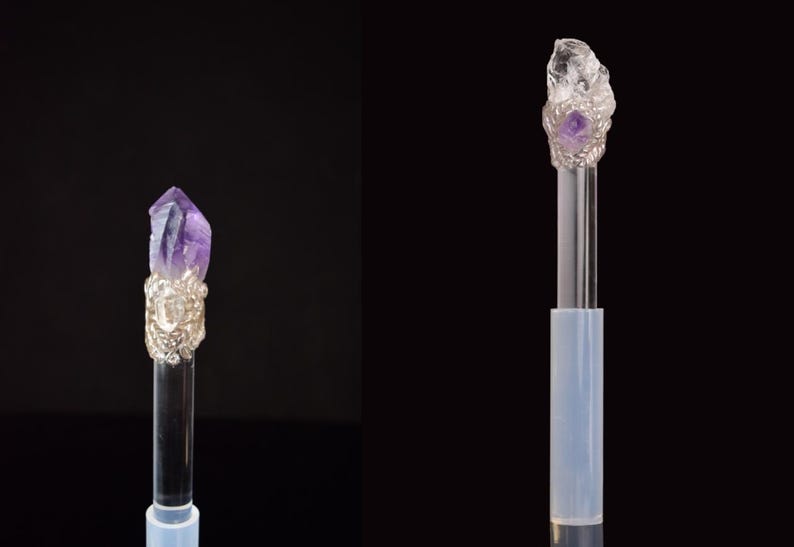 Puede incluir: Dos varitas de cristal con varillas transparentes y adornos de metal plateado. Una varita presenta un cristal de amatista p&uacute;rpura, la otra un cristal de cuarzo transparente. Ambas sobre fondo negro.