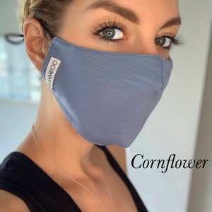 May include: A blue face mask made of bamboo fabric. The mask has a subtle texture and the words "BAMBOO" are printed on the side. The text "Cornflower" is written below the mask.
