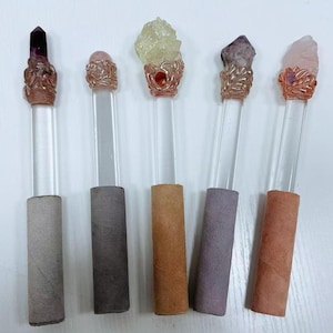 Puede incluir: Cinco varitas de cristal con varillas de acr&iacute;lico transparente y adornos met&aacute;licos decorativos. Cada varita presenta un cristal de diferente color: morado, rosa, amarillo, amatista y cuarzo rosa. Las bases est&aacute;n envueltas en varios tonos de papel.