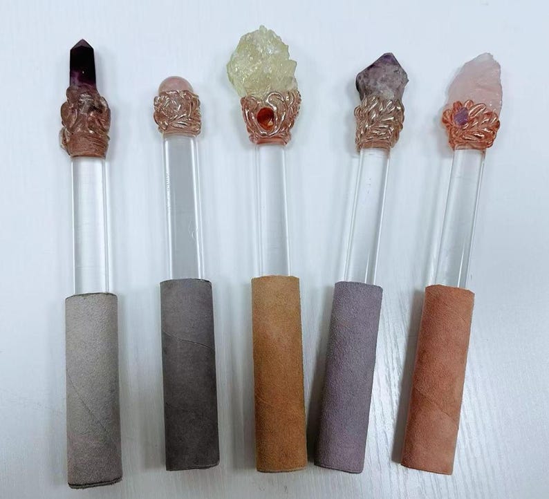Puede incluir: Cinco varitas de cristal con varillas de acr&iacute;lico transparente y adornos met&aacute;licos decorativos. Cada varita presenta un cristal de diferente color: morado, rosa, amarillo, amatista y cuarzo rosa. Las bases est&aacute;n envueltas en varios tonos de papel.
