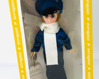 May include: A vintage Effanbee doll in a blue and white outfit with a white scarf and black shoes. The doll has blonde hair and blue eyes. The doll is in a yellow box with the Effanbee logo.