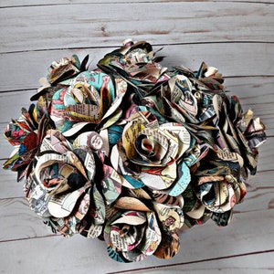 K&ouml;nnte beinhalten: Ein Strau&szlig; handgemachter Papierrosen, die jeweils aus Seiten von Vintage-Comics gefertigt sind. Die Rosen sind in einer kreisf&ouml;rmigen Form angeordnet, wobei die Stiele nach au&szlig;en zeigen. Die Rosen sind in verschiedenen Farben gehalten, darunter Rot, Blau, Gr&uuml;n und Gelb.