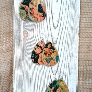 May include: A pair of dangle earrings featuring Wonder Woman comic book art printed on wood. The earrings are teardrop shaped and have silver hooks.