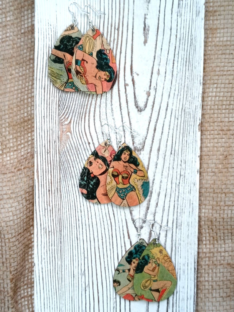 May include: A pair of dangle earrings featuring Wonder Woman comic book art printed on wood. The earrings are teardrop shaped and have silver hooks.