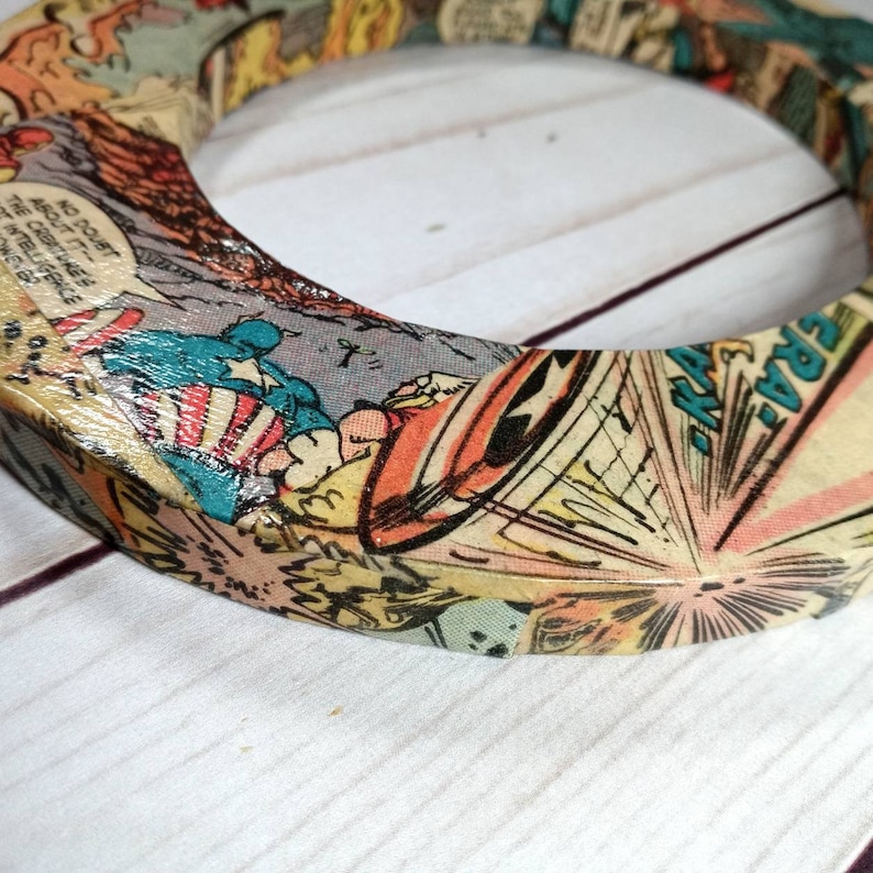 Puede incluir: Un anillo de madera con un dise&ntilde;o de portada de c&oacute;mic. El anillo est&aacute; decorado con una imagen colorida de un superh&eacute;roe volando por el aire. El texto "NO DOUBT ABOUT IT!" es visible en el anillo.