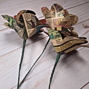 K&ouml;nnte beinhalten: Drei Papierrosen aus alten Comic-Seiten. Die Rosen sind hellbraun mit schwarzem und wei&szlig;em Text und Bildern. Die Stiele sind in gr&uuml;nes Papier gewickelt.