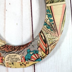 Puede incluir: Un posavasos circular de madera con un dise&ntilde;o de c&oacute;mic que presenta a Capit&aacute;n Am&eacute;rica. El posavasos tiene un esquema de color rojo, blanco y azul y presenta el texto "NO DOUBT ABOUT IT - THE CREATURE'S GOT INTELLIGENCE - HOWEVER".