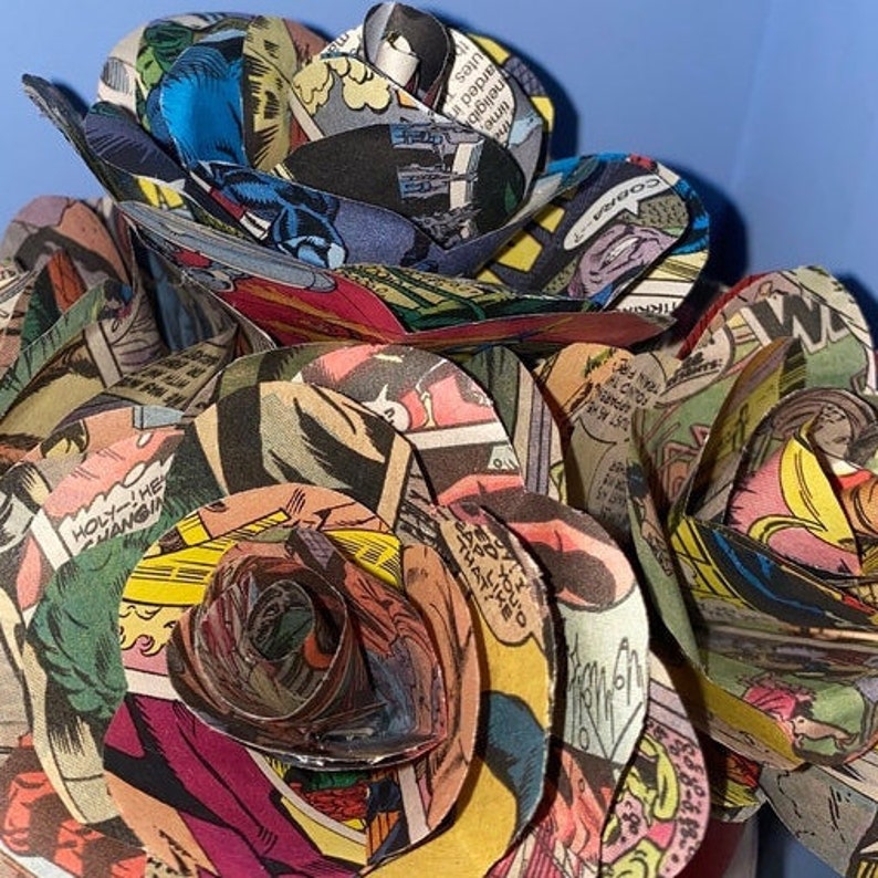 K&ouml;nnte beinhalten: Ein Strau&szlig; Rosen aus Comic-Seiten. Die Rosen sind in verschiedenen Farben, darunter Rot, Gelb und Blau. Die Comic-Seiten zeigen Bilder von Superhelden und anderen Figuren.