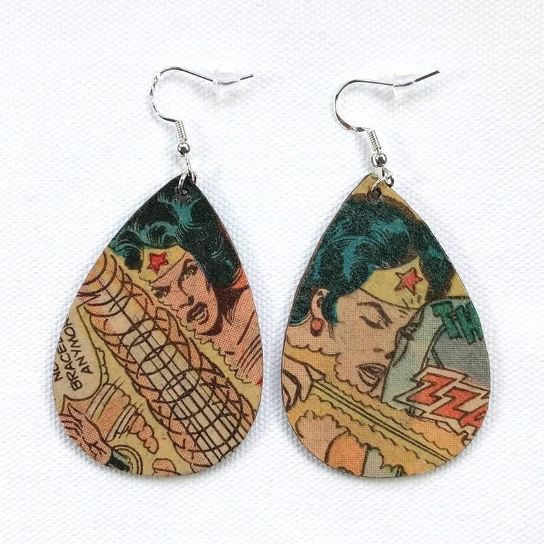May include: A pair of teardrop-shaped earrings featuring a Wonder Woman comic book image. The earrings are made of wood and have silver hooks.