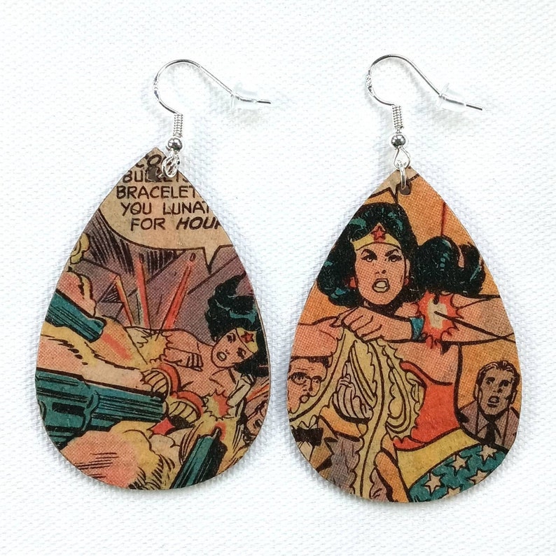 May include: A pair of teardrop-shaped earrings with a comic book design featuring Wonder Woman. The earrings are made of wood and have silver hooks.