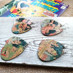 May include: Four pairs of dangle earrings featuring Wonder Woman comic book covers. The earrings are made of wood and have a clear acrylic hook.