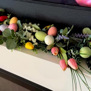 Może przedstawiać: Girlanda wiosenna z zielonymi liśćmi, r&oacute;żowymi, ż&oacute;łtymi i niebieskimi jajkami wielkanocnymi oraz r&oacute;żowymi tulipanami.