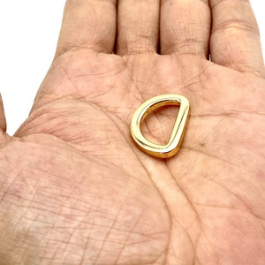 May include: A gold-colored metal D-ring hardware. The ring is smooth and has a polished finish.