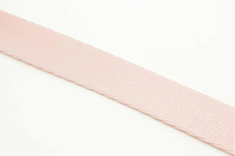 Puede incluir: Primer plano de una cinta de algod&oacute;n de color rosa p&aacute;lido. La cinta tiene un patr&oacute;n de tejido de espiga.