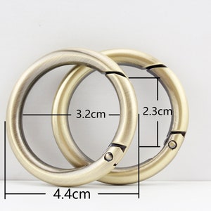 May include: Two gold-toned metal key rings with a spring-loaded clasp. The larger ring measures 4.4 inches in diameter and 3.2 inches in width. The smaller ring measures 2.3 inches in diameter.