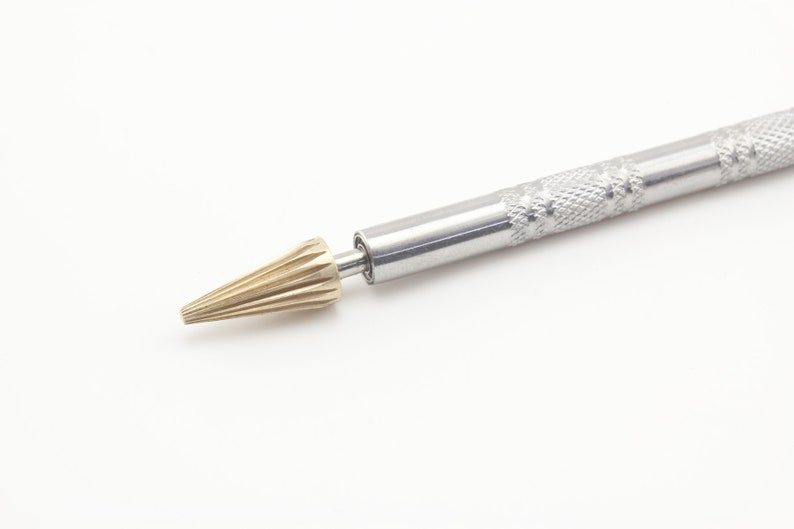 Op de afbeelding: Een zilveren en gouden gereedschap met een getextureerde handgreep en een puntige punt. De punt is ontworpen voor leerbewerking.