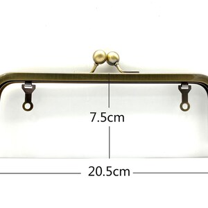 May include: A gold-toned metal purse frame with two round knobs on top. The frame measures 7.5 inches wide and 20.5 inches long.