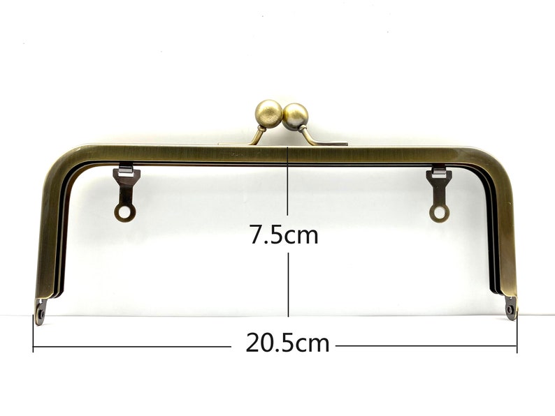 May include: A gold-toned metal purse frame with two round knobs on top. The frame measures 7.5 inches wide and 20.5 inches long.