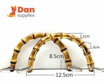 Puede incluir: Dos asas de bolso de bambú marrón con anillos de metal plateado. Las asas miden 8,5 cm de largo, 1,1 cm de ancho y 1,3 cm de alto. Las asas están separadas 12,5 cm.