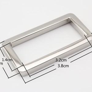 Puede incluir: Hebilla rectangular de metal plateado con las siguientes medidas: 3,8 cm x 3,2 cm x 1,4 cm.