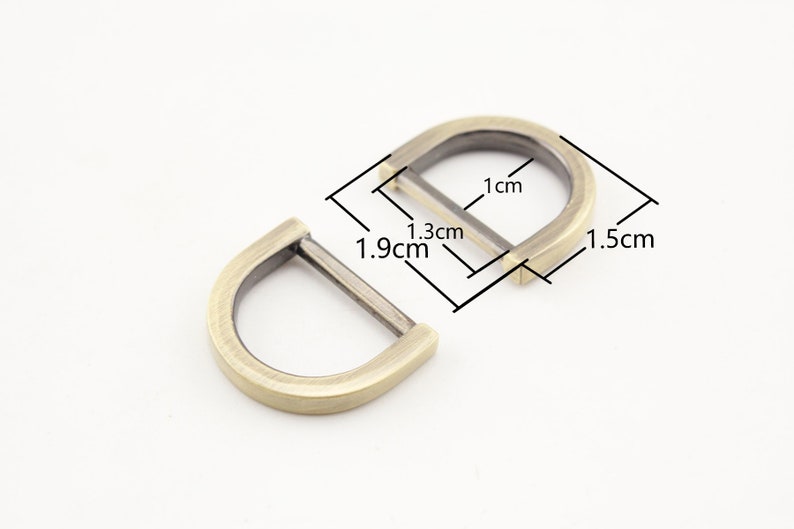 May include: Two antique gold metal D-rings. The larger ring measures 1.5 inches wide and 1.3 inches tall. The smaller ring measures 1.9 inches wide.