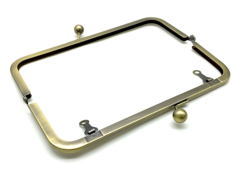 May include: Antique brass-toned metal purse frame with two clasps and two round knobs. The frame is open and ready to be used for a purse or clutch.