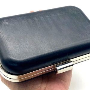 May include: A black clutch purse with a silver metal clasp and a textured surface.