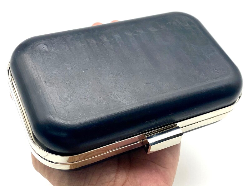 May include: A black clutch purse with a silver metal clasp and a textured surface.