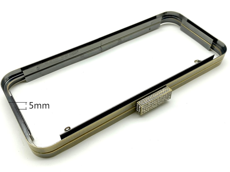 Pu&ograve; includere: Una cornice in metallo dorato per una borsa a mano con una chiusura in strass trasparente. La cornice misura 5 mm di larghezza.