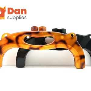 May include: Three plastic bag holder handles. One is black, one is brown with a tortoiseshell pattern, and one is brown with a tortoiseshell pattern and a black handle.