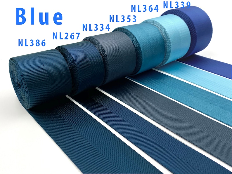 May include: A collection of blue nylon webbing rolls arranged in a row, featuring various shades from dark navy to light sky blue. Each roll is labeled with codes NL386, NL267, NL334, NL353, NL364, and NL339. The fabric has a distinct woven texture.
