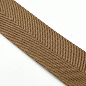 May include: A brown herringbone ribbon with a subtle sheen. The ribbon is woven with a tight, even weave.