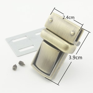 May include: Antique brass-coloured metal clasp with a rectangular shape and a rounded edge. The clasp measures 3.9 cm by 2.4 cm and comes with two screws.