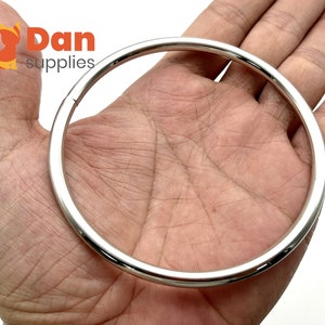 Könnte beinhalten: Ein silberner Metallring mit einem Durchmesser von etwa 7,6 cm wird in der Hand einer Person gehalten. Der Ring ist glatt und hat eine polierte Oberfläche.