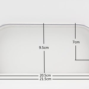 Op de afbeelding: Zilveren metalen tasthandvat met een breedte van 9,5 cm, een hoogte van 7 cm en een lengte van 20,5 cm.