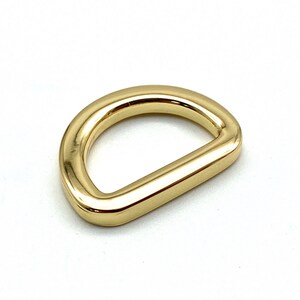 May include: A gold-colored metal D-ring hardware. The ring is smooth and shiny.