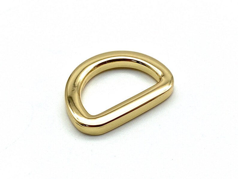 May include: A gold-colored metal D-ring hardware. The ring is smooth and shiny.
