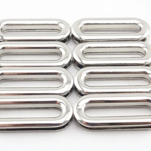Op de afbeelding: Acht zilveren ovale metalen oogjes met een gladde afwerking. De oogjes hebben een gat in het midden.