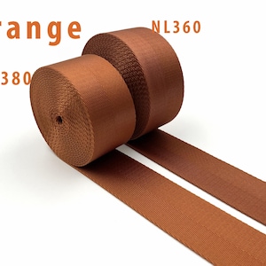 May include: Two rolls of orange nylon webbing tape are displayed, each featuring a distinct herringbone weave pattern. The text "Orange" is visible at the top left, with "NL380" below it and "NL360" positioned near the second roll of webbing.