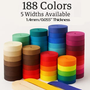 May include: Stacks of colorful ribbon rolls in various shades, including green, blue, red, and yellow. The image also shows loose ribbon strips in cream, yellow, and blue. Text at the top reads "188 Colors, 5 Widths Available, 1.4mm/0.055" Thickness."