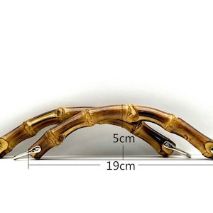 Może przedstawiać: Dwa brązowe uchwyty bambusowe ze srebrnymi metalowymi kółkami. Uchwyty są zakrzywione i mają 5 cm wysokości i 19 cm szerokości.
