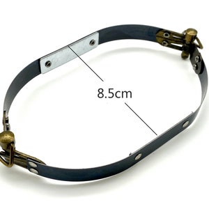 Könnte beinhalten: Ein schwarzer Metallring mit zwei Messingverschlüssen. Der Ring hat einen Durchmesser von 8,5 cm.