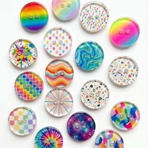 Könnte beinhalten: Eine Sammlung bunter, personalisierter Nähknöpfe. Die Knöpfe weisen verschiedene Designs auf, darunter Regenbogenverläufe, Tupfen, Wirbel und Blumenmuster. Der Text "Personalized sewing Buttons" steht oben.