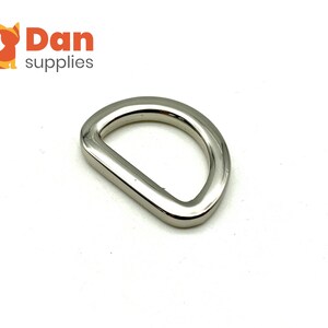 May include: A silver-toned metal D-ring hardware. This type of ring is often used for attaching straps, leashes, or other accessories.