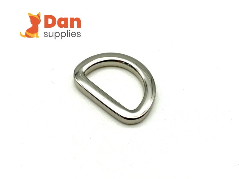 May include: A silver-toned metal D-ring hardware. This type of ring is often used for attaching straps, leashes, or other accessories.